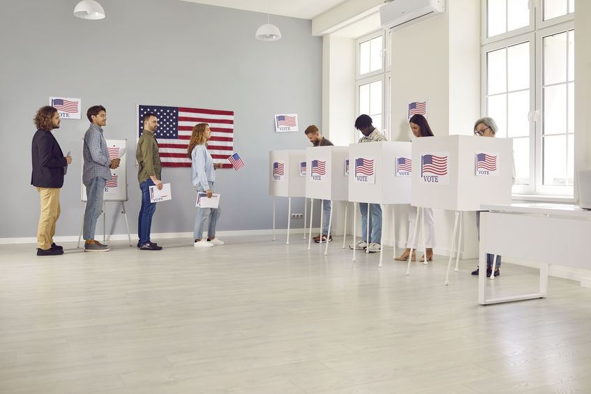 Voters stand in line along voting booths at polling station waiting for other people to vote.