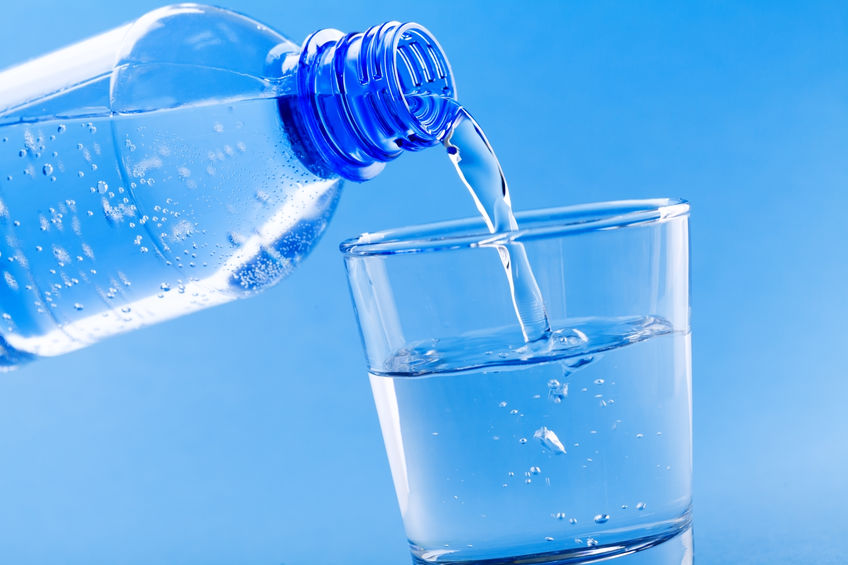 Pouring drinking water from bottle into glass on blue background.