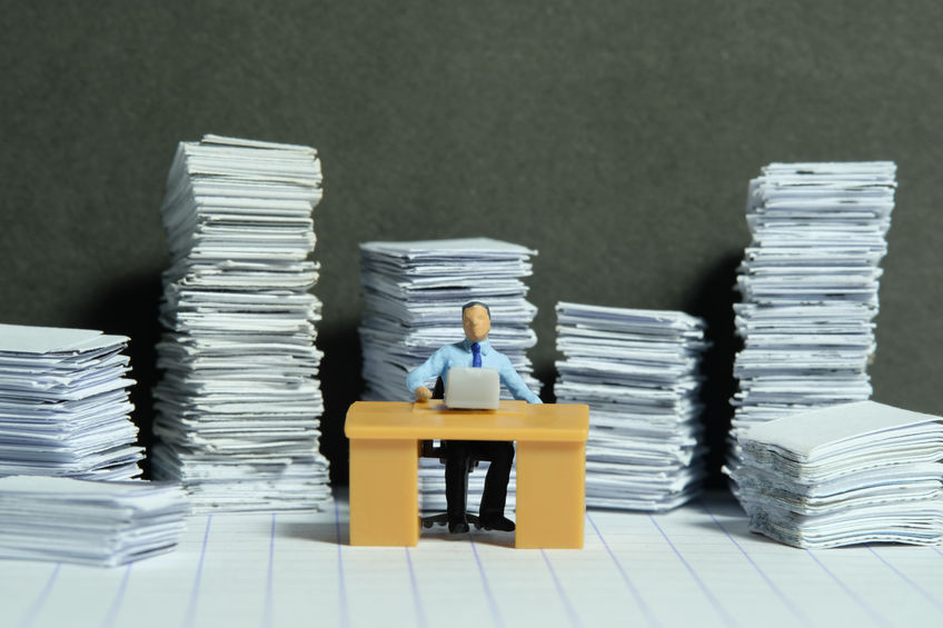 Miniature tiny people toy figure photography. Overload and work overtime concept. A businessman seat on a desk with pile of document