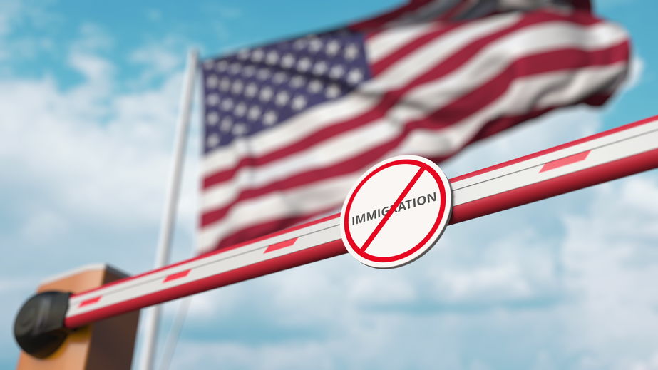 Closed boom barrier with stop immigration sign against the American flag. Border closure or immigration ban in the USA. 3D rendering