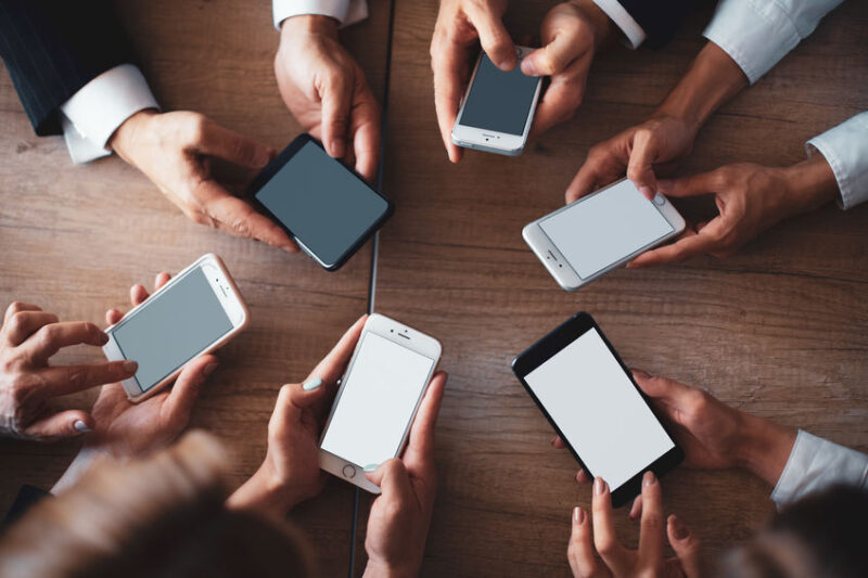 Office workers work on phones. Mobile meeting concept. Close up of human hands using smartphones on wooden table. Top view