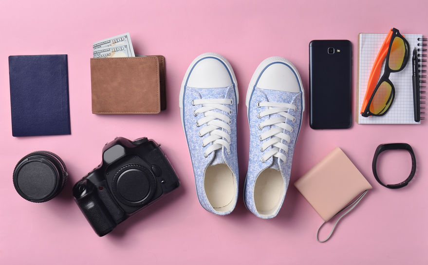 Gadgets and accessories layout on a pink pastel background. Sneakers, photographic equipment, purse with dollars, smart clock, smartphone, notebook, sunglasses. Concept of travel, objects, top view