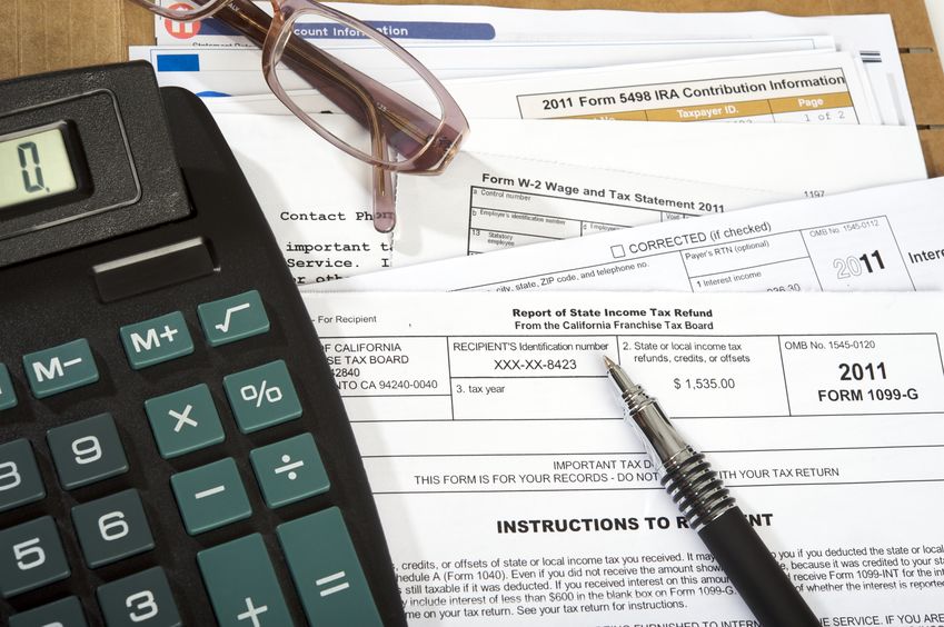 11945715 multiple taxes forms on a desk with glasses, pen and calculator