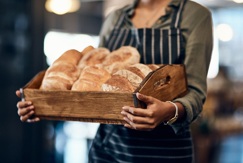 The crispiest buns around town. a woman holding a selection of freshly baked breads in her bakery.